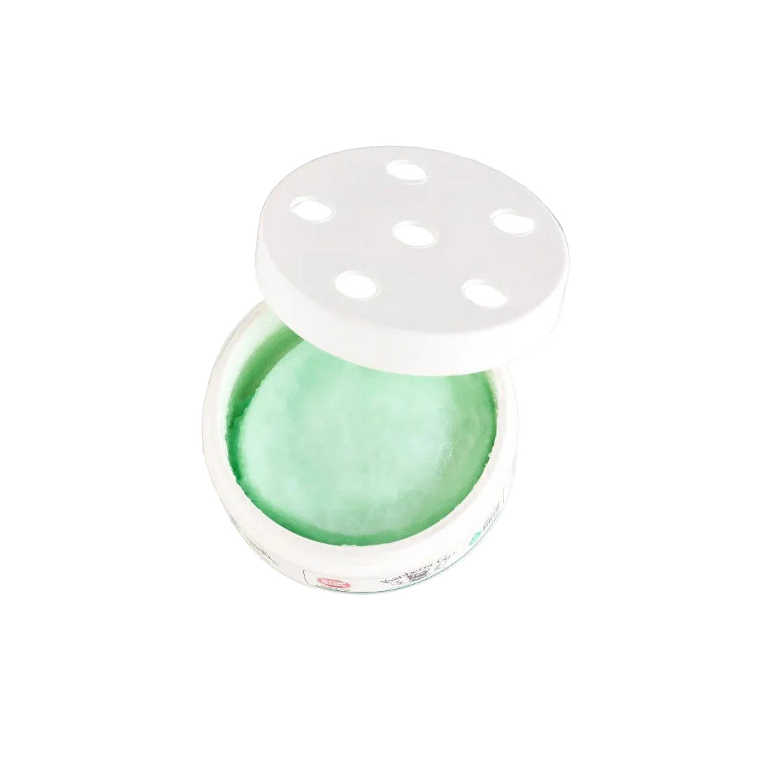 A round white container with its lid off, showing a pale mint green solid or gel-like product inside, placed on a white marble surface.